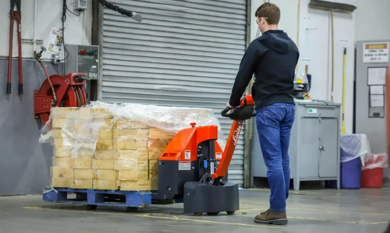 Linde MT electric pallet jack transporting palletized lumber inside an industrial warehouse